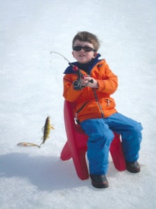 A little boy sits on the ice with a caught fish